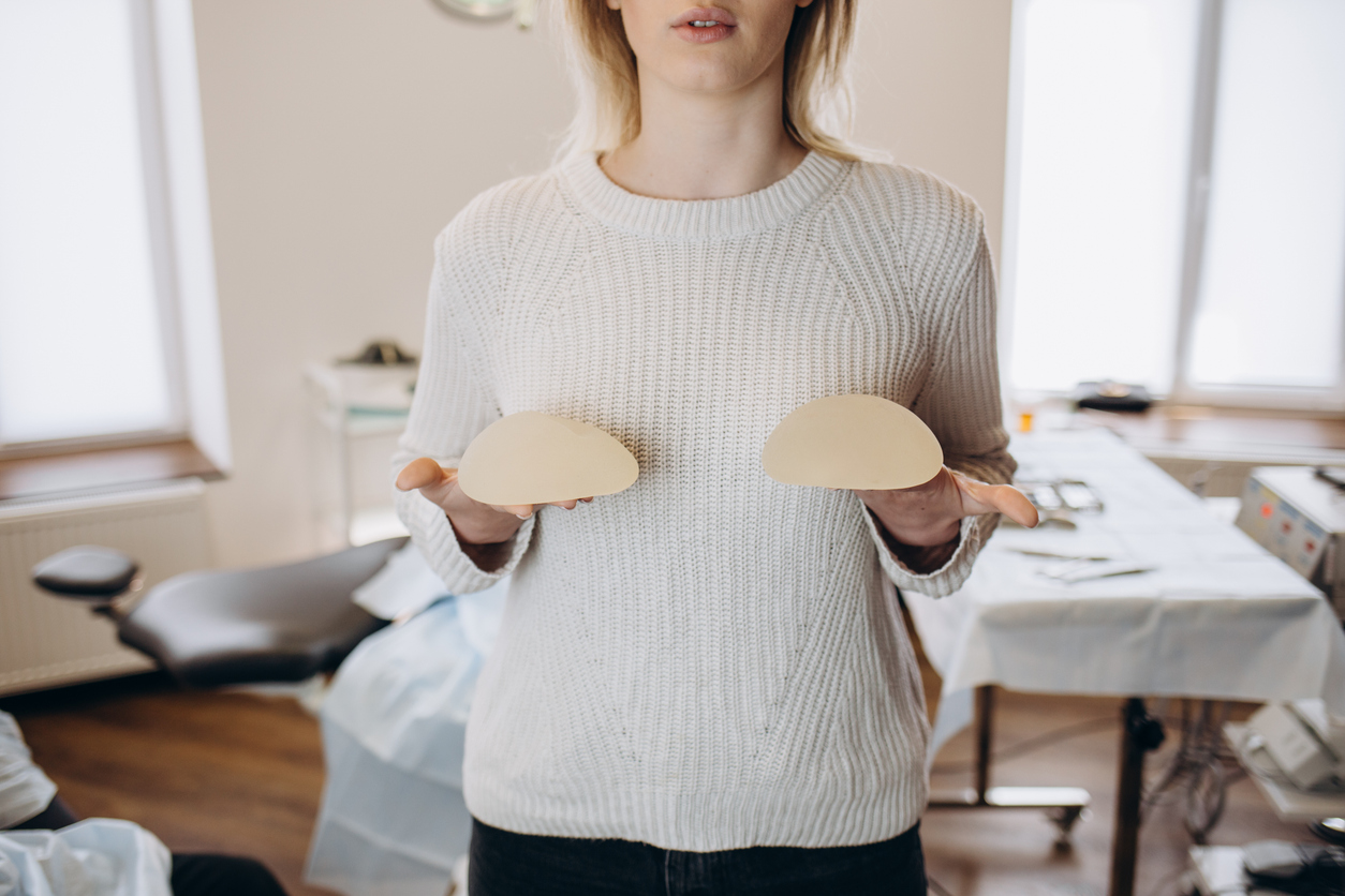 Close up of a woman holding breast implants in front of her, debating on implant size and shape.